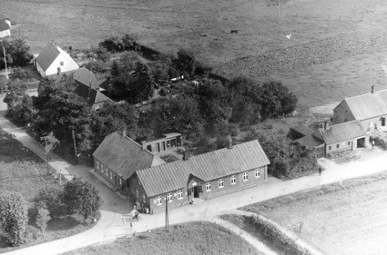 Forgrund: Staksrode Brugsforening. Til højre smedjen og centralen, bagved mellem træerne skolen og i baggrunden Den Gamle Skole ca. 1955.
